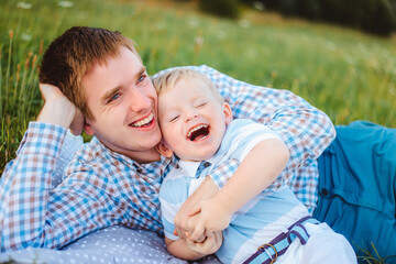 Dad and his son are in nature in the summer. A happy family lies on the grass, embrace and laugh in the rays of the sun.