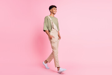 Profile photo of cheerful guy step look empty space wear green t-shirt beige overall sneakers isolated pink color background