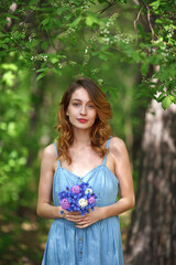 beautiful girl in a denim sundress walks with a bouquet of hyacinths in the garden, spring mood