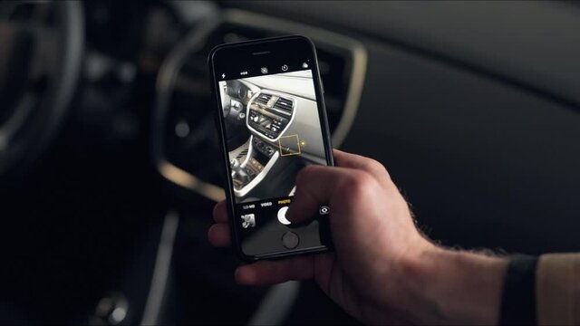 Close-up of male hands and smartphone screen taking pictures of car inside