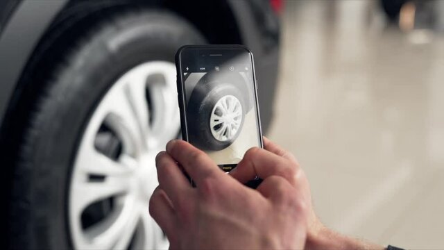 Close-up of male hands taking pictures with smartphone of new wheel in car