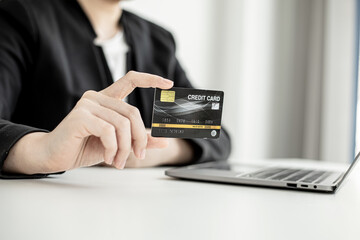 A business woman holds a credit card to make payments on the website where she is shopping online. Concept of using credit cards to pay for goods and services on online websites.