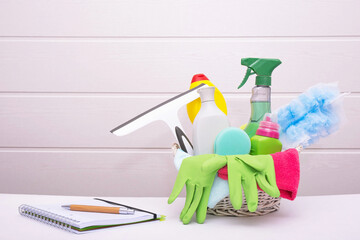 a basket with cleaning and disinfectants for cleaning the house with green gloves and brushes, a notebook with a pen