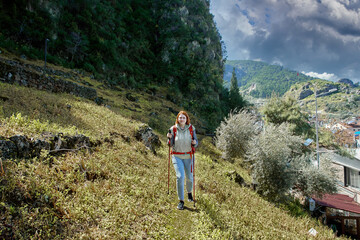 Young white woman uses walking pole as she climbs hillside near resort town of Fethiye in Turkey.