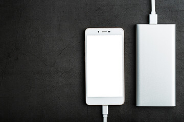 White Smartphone is being charged from the Power Bank on a black background. Top view, free space