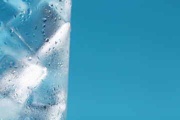 A glass with ice water and ice cubes on a blue background.