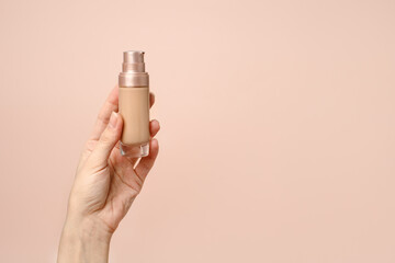 Hand holding makeup liquid found, Applying foundation for makeup. Woman's hands with neutral manicure holding bottle of concealer or toner foundation, copy space, banner, flyer - 425591347
