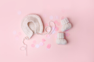 Bonnet and booties on a pink background. Handmade clothes for a newborn, decorative confetti. Newborn baby gift concept, mom's day, first birthday, first wardrobe, outfit