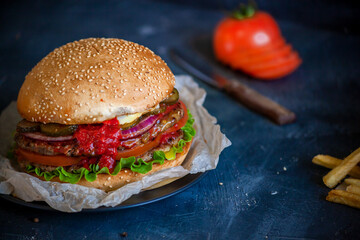 Hamburger with a knife lies on a board on a dark background