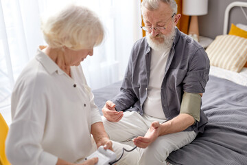 Obraz premium Senior woman controlling blood pressure of husband using stethoscope