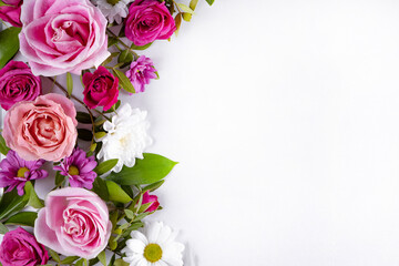 Beautiful summer flowers on the white background with empty space for text. Pink roses and white daisies top view