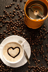 A coffee grinder, a cup of coffee with the drawing of a chocolate heart and a lot of coffee beans on the table