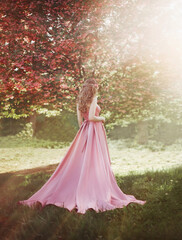 Spring woman walks in blooming sakura tree garden. Medieval long-haired girl, mysterious blonde...