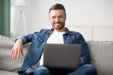 Cheerful middle-aged man using laptop while resting at home