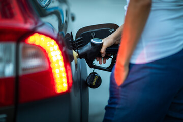 Young female driver refueling her car at night with gas(color toned image; shallow DOF)