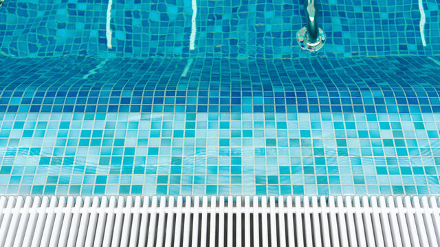Top view of empty pool with hydro massage in swimming pool with blue mosaic tiles and drain bars. Transparent calm pool water background for photo collage. Smooth entrance to the pool.