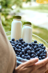 Blueberries and a bottle of yogurt in the hands of a woman. Natural organic berries. Fresh blueberries close up. Delicious summer berry. Proper nutrition. Berries for dessert. Healthy lifestyle