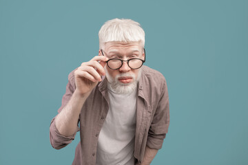 Poor eyesight. Albino man in eyeglasses squinting eyes, having bad sight, trying to see something over blue background