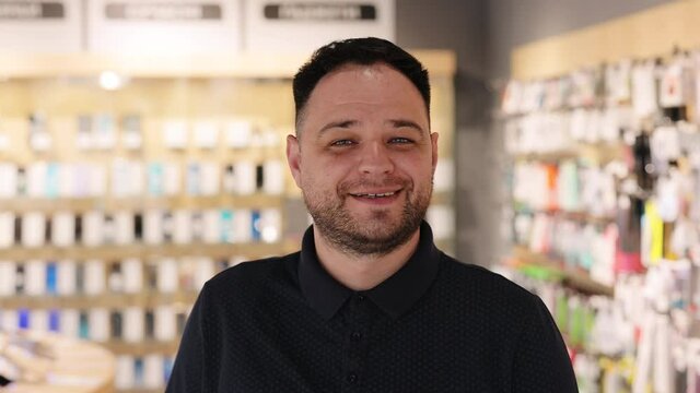 Close up face view business portrait. Smiling caucasian millennial seller man in electronics store looking at camera. Happy confident male shop assistant at gadget store.