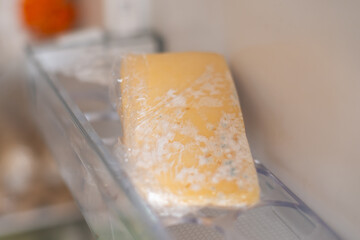 Moldy cheese wrapped in cling film in the refrigerator. Incorrect storage, spoiled product, expired...