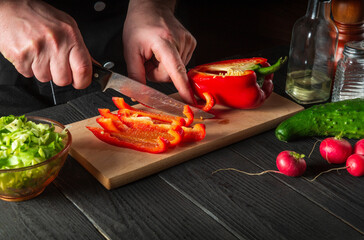 Close-up of chef hands cutting peppers on cutting board. Professional preparation of salad in the kitchen in a restaurant or cafe