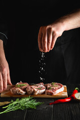 Chef sprinkles the meat with salt. Preparing meat before baking. Working environment in the kitchen of restaurant or cafe