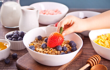 Healthy breakfast. Granola, muesli with fresh berries. Child hand take a strawberry.