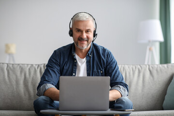 Smiling matured man working online, using laptop and headset