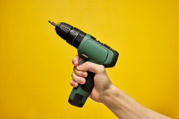 Battery screwdriver or drill in hands isolated over yellow background