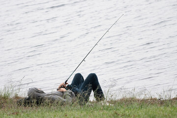 Obraz na płótnie Canvas Fisherman lying on wet grass. Fishing as a relaxing outdoor hobby. Concept of patience and rewards of waiting.