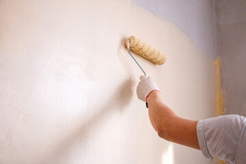 mans hand in cloth glove with paint roller applies fresh paint and primer to wall surface. process...