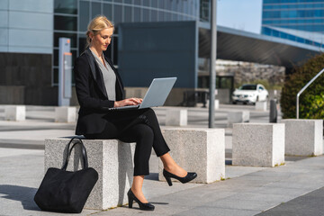 Mujer rubia ejecutiva sentada con el ordenador portátil en centro de negocios con bolso en el suelo
