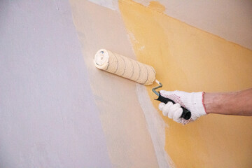 mans hand in cloth glove with paint roller applies fresh paint and primer to wall surface. process...