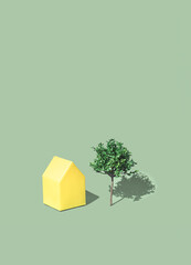 Minimal residential real estate concept with a town house and a tree on a illuminating yellow background. Happy sunny home and eco friendly living idea.
