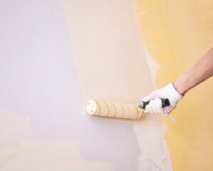 mans hand in cloth glove with paint roller applies fresh paint and primer to wall surface. process of applying water-based paint and primer with paint roller on surface for  interior design of room.