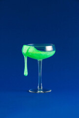 Bold vibrant neon green cocktail drink on dark blue background. Surreal minimal party concept. Celebration idea with champagne glass.