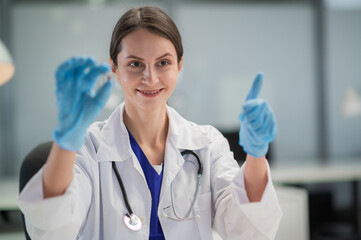 A young female doctor in blue medical gloves shows a patient a capsule with a new drug. Portrait on...