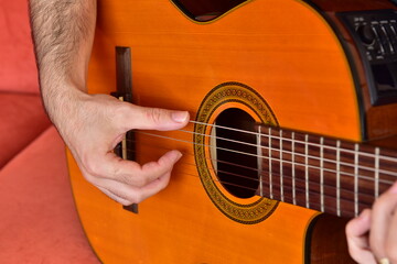 Fototapeta premium Boy playing music on acoustic guitar sitting on red sofa.