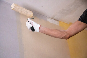 mans hand in cloth glove with paint roller applies fresh paint and primer to wall surface. process...