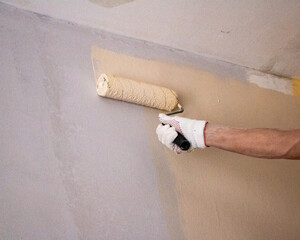 mans hand in cloth glove with paint roller applies fresh paint and primer to wall surface. process...