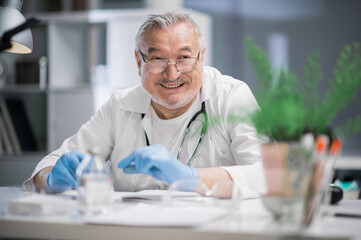 Portrait of a smiling adult doctor with a stethoscope around his neck at his desk in the hospital