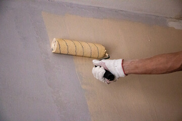 mans hand in cloth glove with paint roller applies fresh paint and primer to wall surface. process...