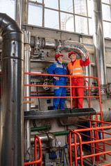 Maintenance Engineer Standing Next to Oil Worker in Oil Refinery with Large Piping