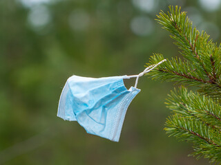 Medical disposable blue protective mask floats in the wind on the pine branches, coronavirus Covid-19 virus waste. Garbage collection. Green planet earth. Medical waste