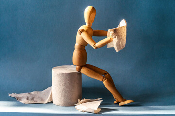 Wooden figure sit on a roll of toilet paper and reading the newspaper