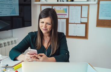 Smiling female professor having break with online class and using her mobile phone to send text...