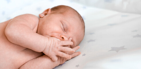 Closeup portrait of Newborn baby sleeping on white blanket. Soft focus. A one weeks old infant is sleeping tightly on her side in bed. 10 days old child. Panoramic banner with copy space.