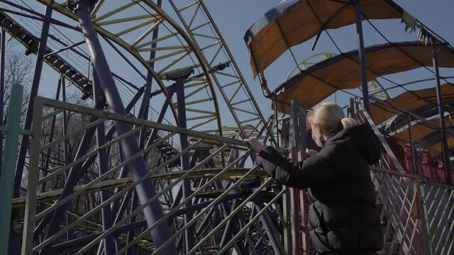 Woman standing in abandoned amusement park, rust-covered roller coaster
