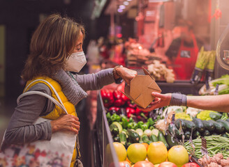 woman in yellow vest and mask buying Mediterranean fruits and vegetables in a traditional market. healthy food and Mediterranean diet of proximity.