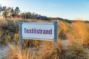 Strand, Meer , Dünen und ein Schild mit dem Hinweis auf 
den Beginn des Textilstrandes